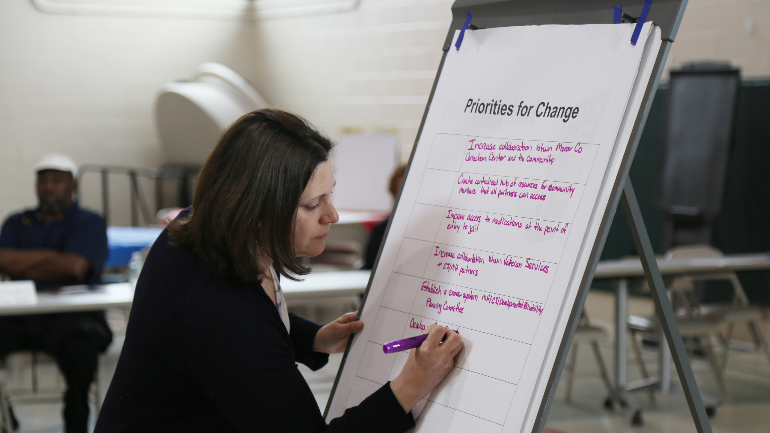 Woman writing at a large easel with a pink pen.