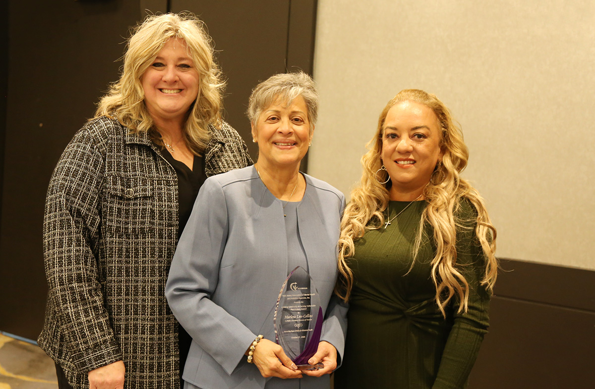 Mary Pettrow, Marlene Lao-Collins and Lisa Merritt standing in a row. The women are smiling and Marlene is holding a glass award. 