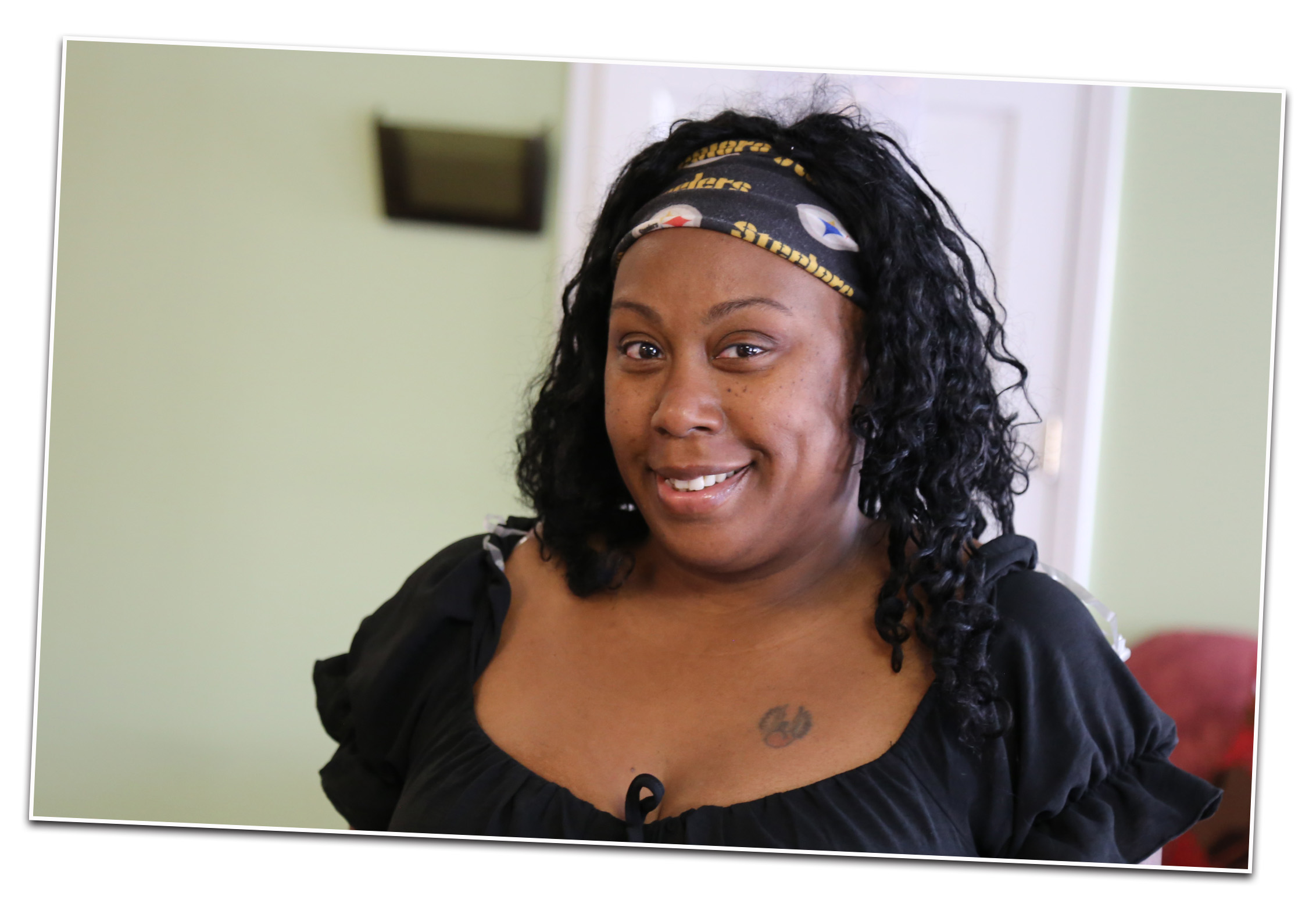 A young black woman wearing a Pittsburgh Steelers headband and black blouse smiling. 